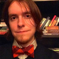 A headshot of Andrew Kulak earing an orange and maroon Virginia Tech bowtie in front of a bookshelf.
